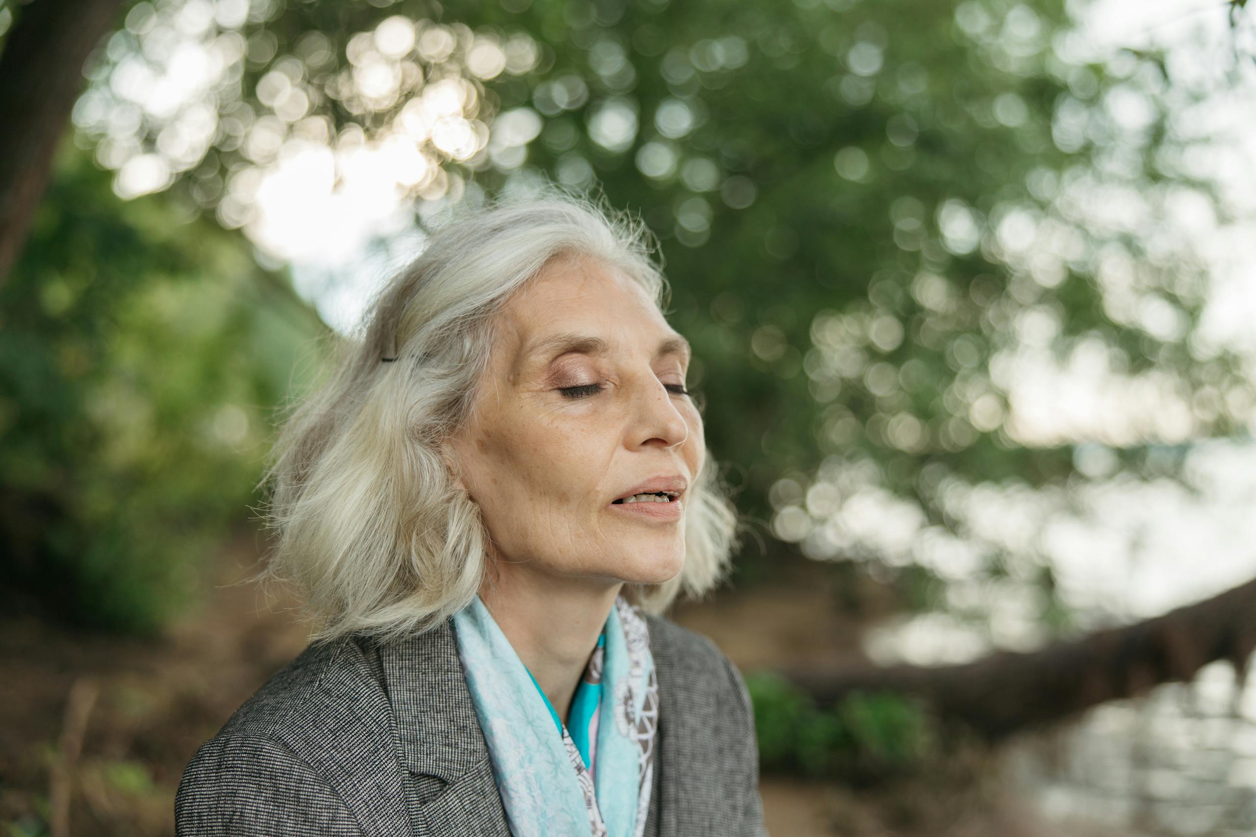 Serene elderly woman meditating outdoors with eyes closed, enjoying nature.