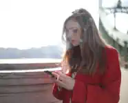 Portrait einer Frau in Rot, die im Freien raucht und eine Nachricht tippt