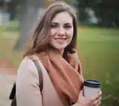Portrait einer lächelnden Frau im Park, die einen Kaffeebecher in der Hand hält