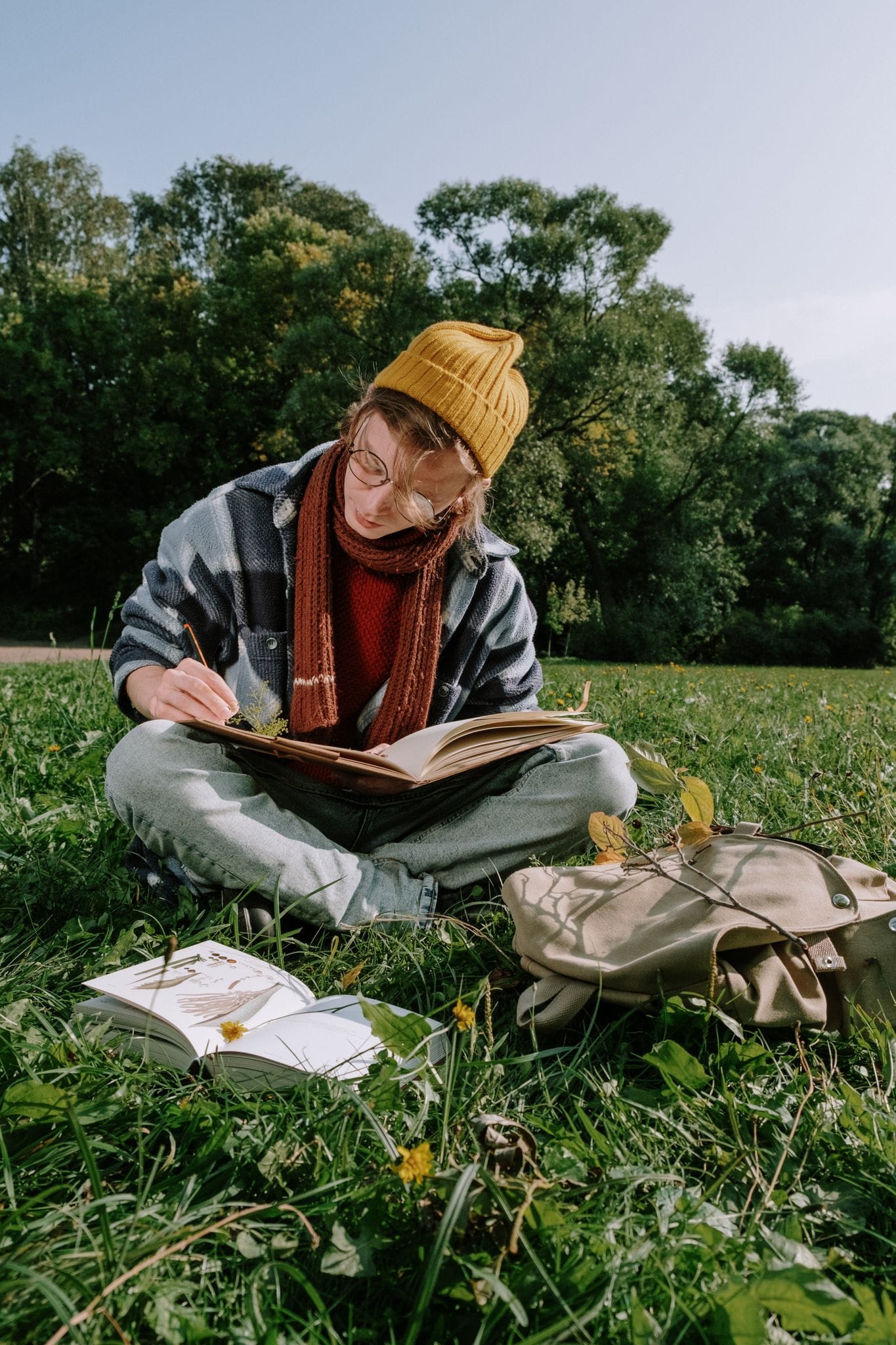 Ein junger Erwachsener sitzt auf dem Rasen, schreibt in ein Buch und genießt einen sonnigen Tag im Park.