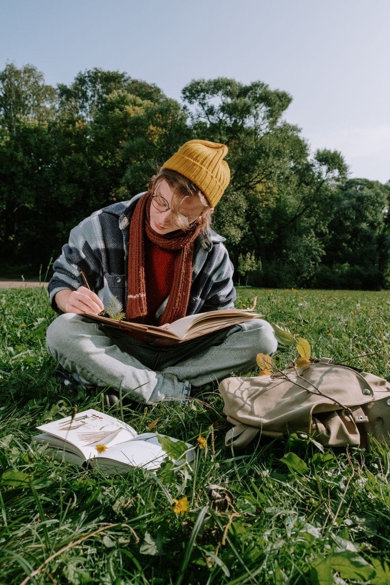 Ein junger Erwachsener sitzt auf dem Rasen, schreibt in ein Buch und genießt einen sonnigen Tag im Park.