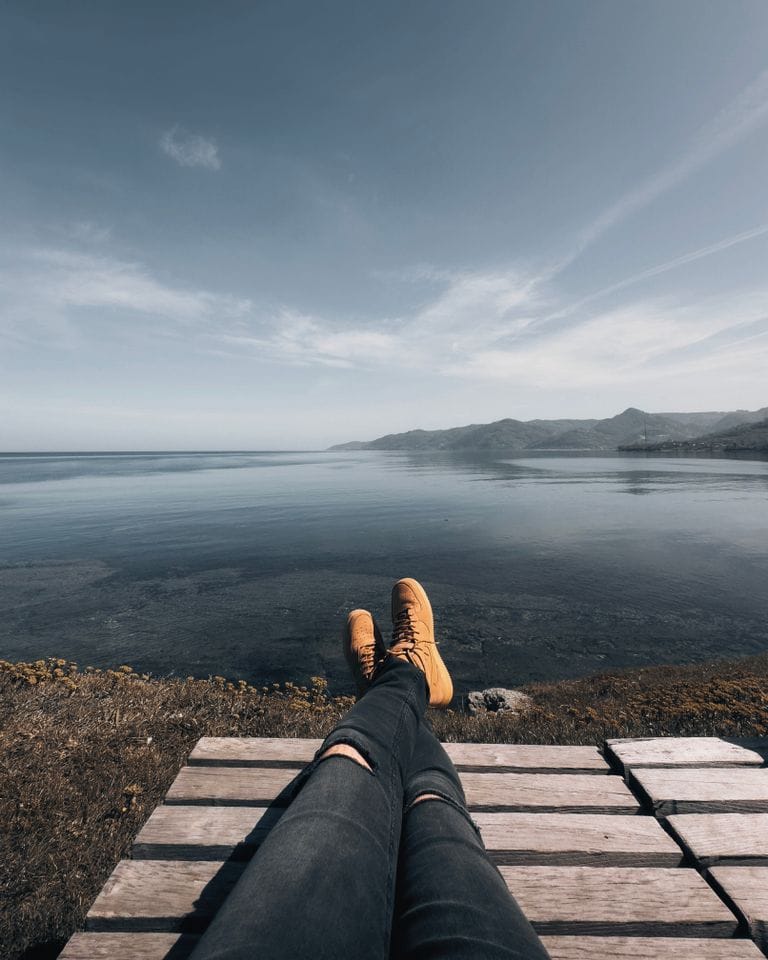 Person relaxing on a bench overlooking the tranquil ocean on a sunny day.